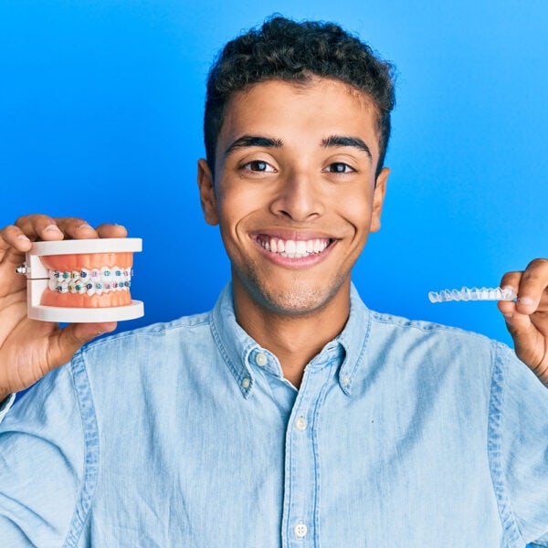 Junger Mann hält feste Zahnspange und Aligner zum Vergleich, Zahnbegradigung