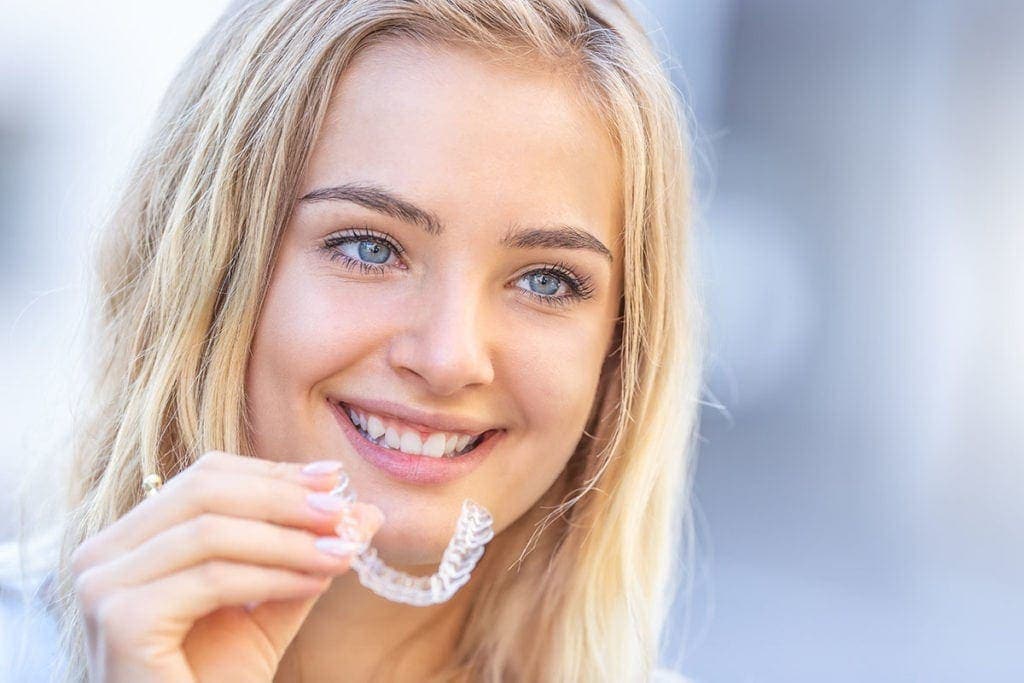 Lächelnde Frau hält transparente Zahnspange